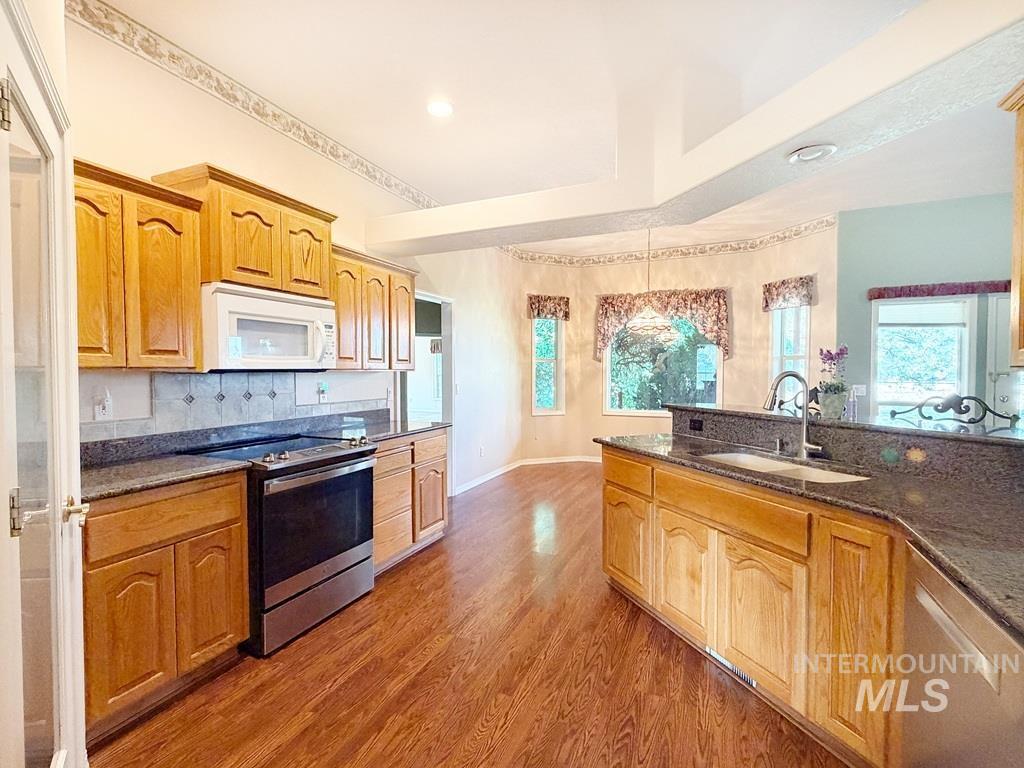 5875 Diamond Ridge Way Nampa, ID 83686 - Photo 12 of 32 Spacious kitchen featuring warm wood cabinetry, stainless steel appliances, dual countertop work surfaces with dark stone counters, and abundant natural light from multiple windows