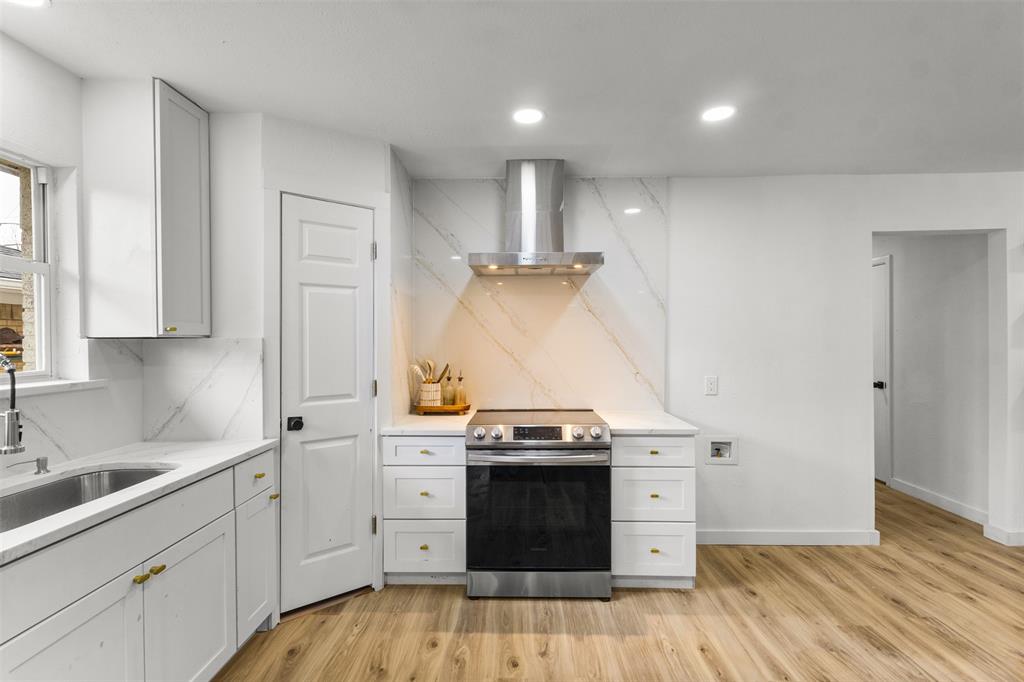 1917 South Vernon Avenue Dallas, TX 75224 - Photo 8 of 28 Modern kitchen featuring white cabinetry with gold-tone hardware, a stainless steel range with a matching range hood, and a marble-look backsplash