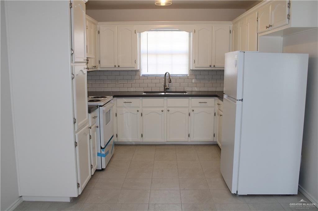 1408 Pine Street, Unit C Weslaco, TX 78596 - Photo 3 of 9 Kitchen with white appliances, dark countertops, tasteful backsplash, white cabinetry, and light tile patterned flooring