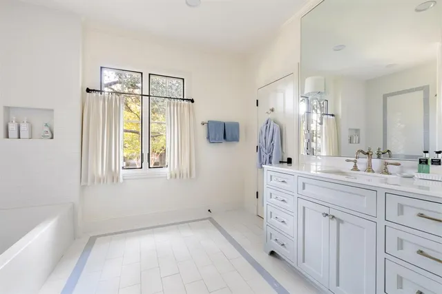 a spacious bathroom with a double vanity sink a mirror a bathtub and next to a window