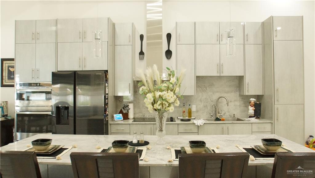 414 Ric Mar Street Edinburg, TX 78541 - Photo 13 of 36 Contemporary kitchen featuring extensive cabinetry, stainless steel appliances, a double oven, a refrigerator with a water dispenser, and a kitchen island with a light-colored countertop