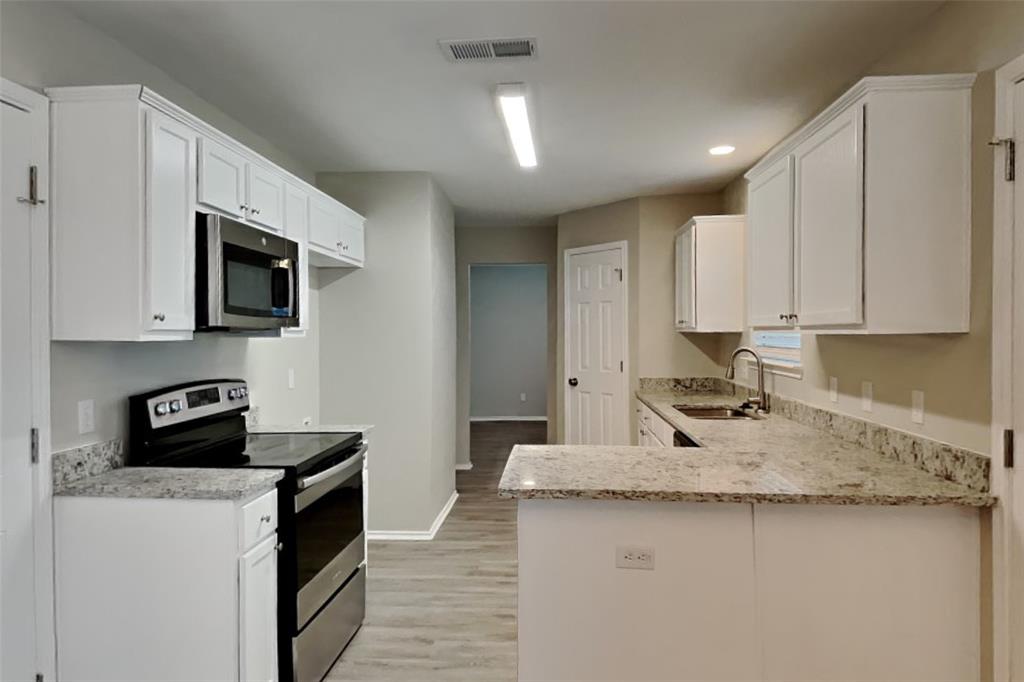 3925 Cane River Road Fort Worth, TX 76244 - Photo 4 of 21 Kitchen featuring stainless steel appliances, a peninsula, light stone counters, white cabinets, and light wood-style flooring