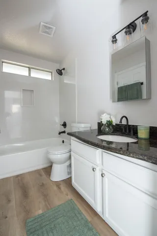 a bathroom with a granite countertop sink a toilet a mirror and bathtub
