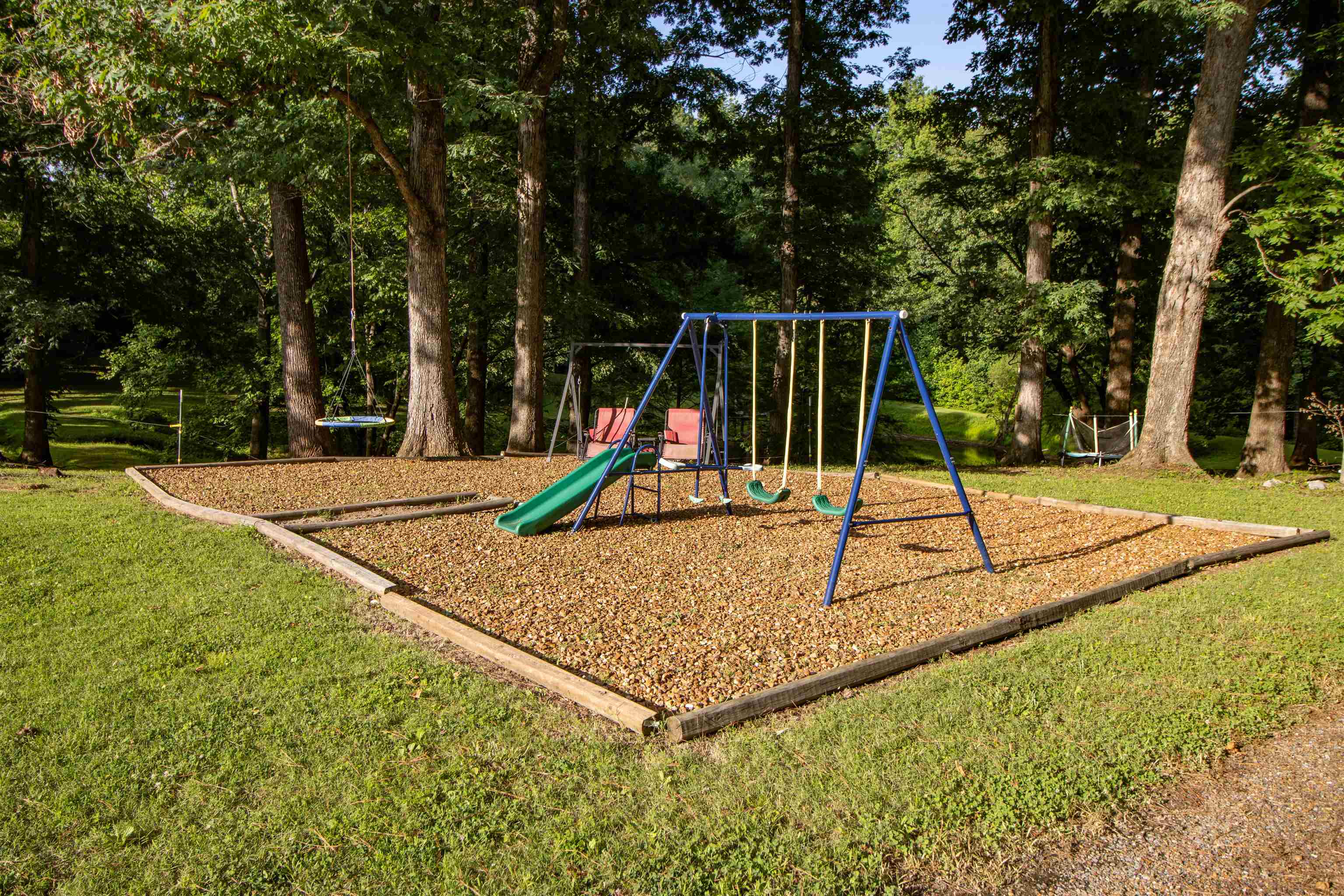 120 Craig Road Ripley, TN 38063 - Photo 28 of 38 Outdoor play area featuring a swing set with slide, a separate tire swing, and a wood chip surface, all surrounded by mature trees and a grassy lawn