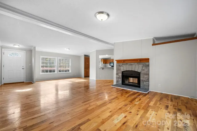 a view of an empty room with wooden floor fireplace and a window