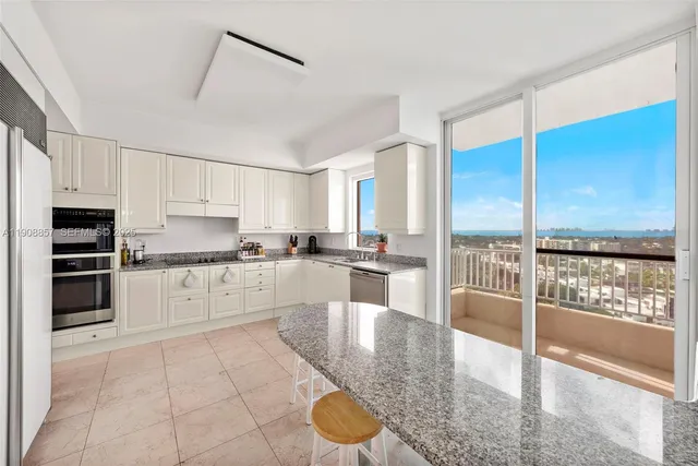 a large white kitchen with granite countertop a large counter top stainless steel appliances and cabinets