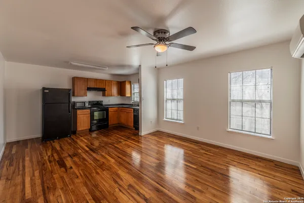 a living room with stainless steel appliances wooden floors and kitchen view