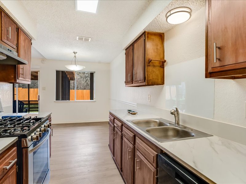 3908 Holt Drive Austin, TX 78749 - Photo 12 of 22 Kitchen with stainless steel gas range, wood finish cabinetry, a textured ceiling, light wood-type flooring, and dishwasher
