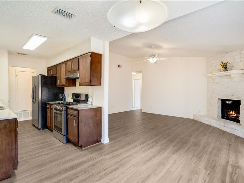 3908 Holt Drive Austin, TX 78749 - Photo 13 of 22 Kitchen featuring stainless steel appliances, light countertops, light wood-type flooring, a stone fireplace, and a textured ceiling