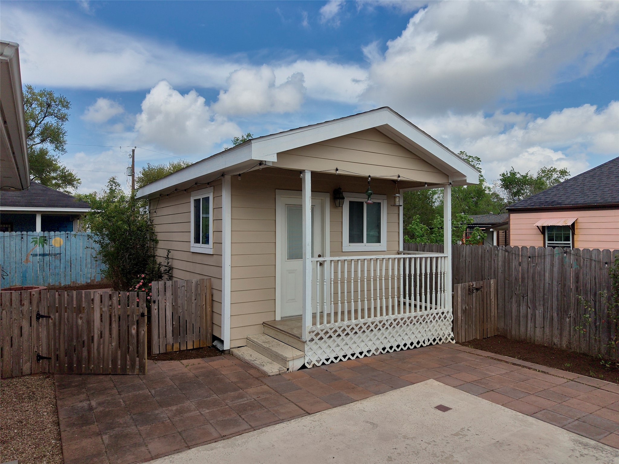 4219 Redbud Street Houston, TX 77051 - Photo 21 of 25 This photo showcases a small, standalone guest house with a charming front porch and beige siding. It's set within a fenced yard, offering privacy and a cozy outdoor area. Ideal for a home office.