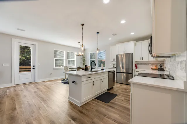 a kitchen with stainless steel appliances kitchen island granite countertop a refrigerator a stove top oven a sink dishwasher and white cabinets with wooden floor