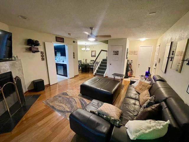 Living room with wood finished floors, stairs, a textured ceiling, a tiled fireplace, and a chandelier