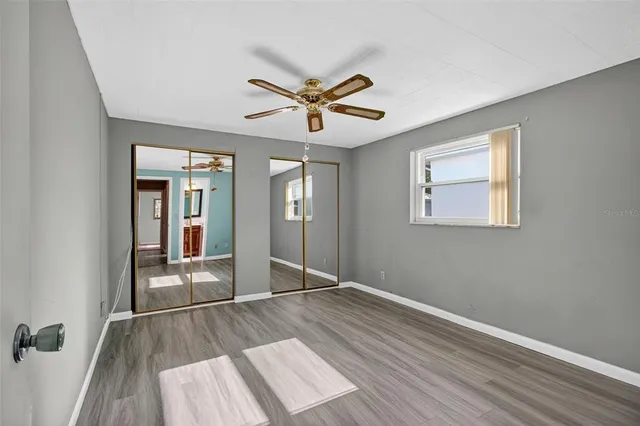 an empty room with wooden floor a ceiling fan and windows