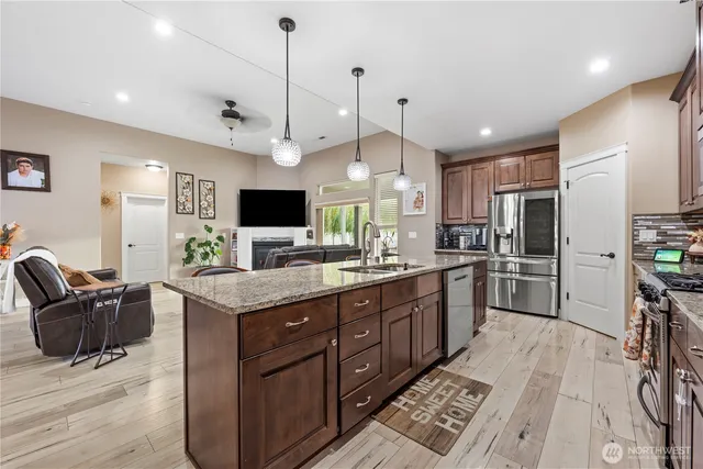 a large kitchen with stainless steel appliances kitchen island granite countertop a stove top oven a sink dishwasher a dining table and chairs with wooden floor