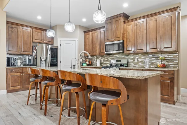 a kitchen with stainless steel appliances granite countertop a stove top oven a refrigerator a sink and chairs