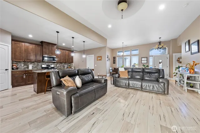 a living room with stainless steel appliances furniture wooden floor and a kitchen view