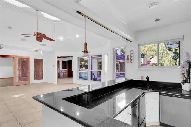 a large hall with stainless steel appliances granite countertop a sink dishwasher a stove a dining table and chairs with wooden floor