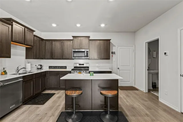 a kitchen with stainless steel appliances a sink a stove a refrigerator cabinets and chairs