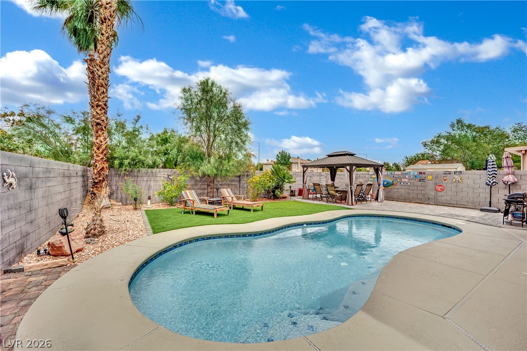 1724 Millstream Way Henderson, NV 89074 - Photo 35 of 60 A tranquil backyard oasis features a freeform swimming pool, mature palm trees, and a shaded outdoor dining area.