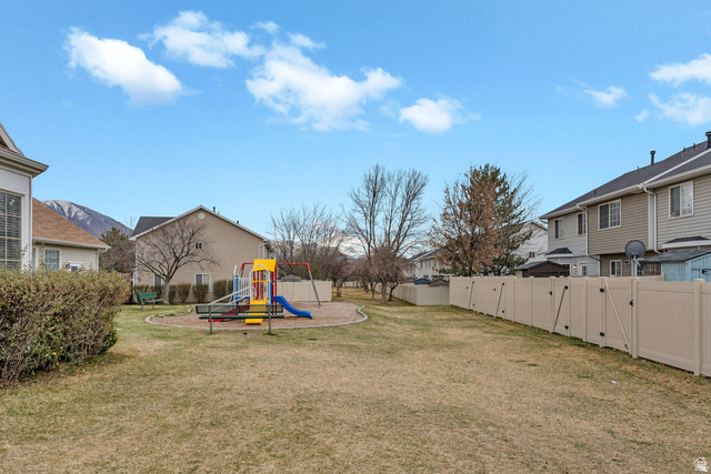 986 Independence Avenue Provo, UT 84604 - Photo 26 of 29 Expansive grassy area featuring a children's play structure with slides and swings, surrounded by a light-toned privacy fence
