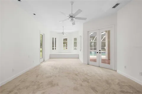 an empty room with chandelier fan and windows