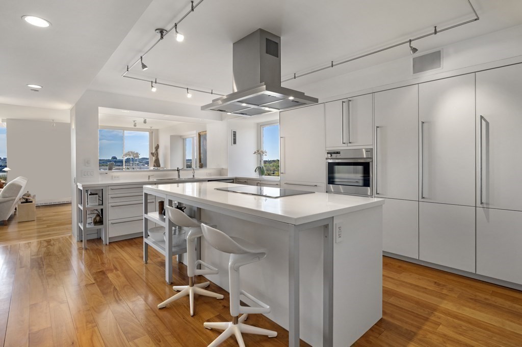 975 Memorial Drive, Unit 906 Cambridge, MA 02138 - Photo 8 of 37 a kitchen with stainless steel appliances kitchen island a table chairs in it and wooden floors