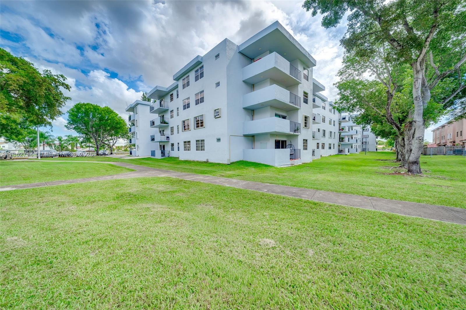1221 Southwest 122nd Avenue, Unit 215 Miami, FL 33184 - Photo 4 of 57 a view of a big building with a big yard and large trees