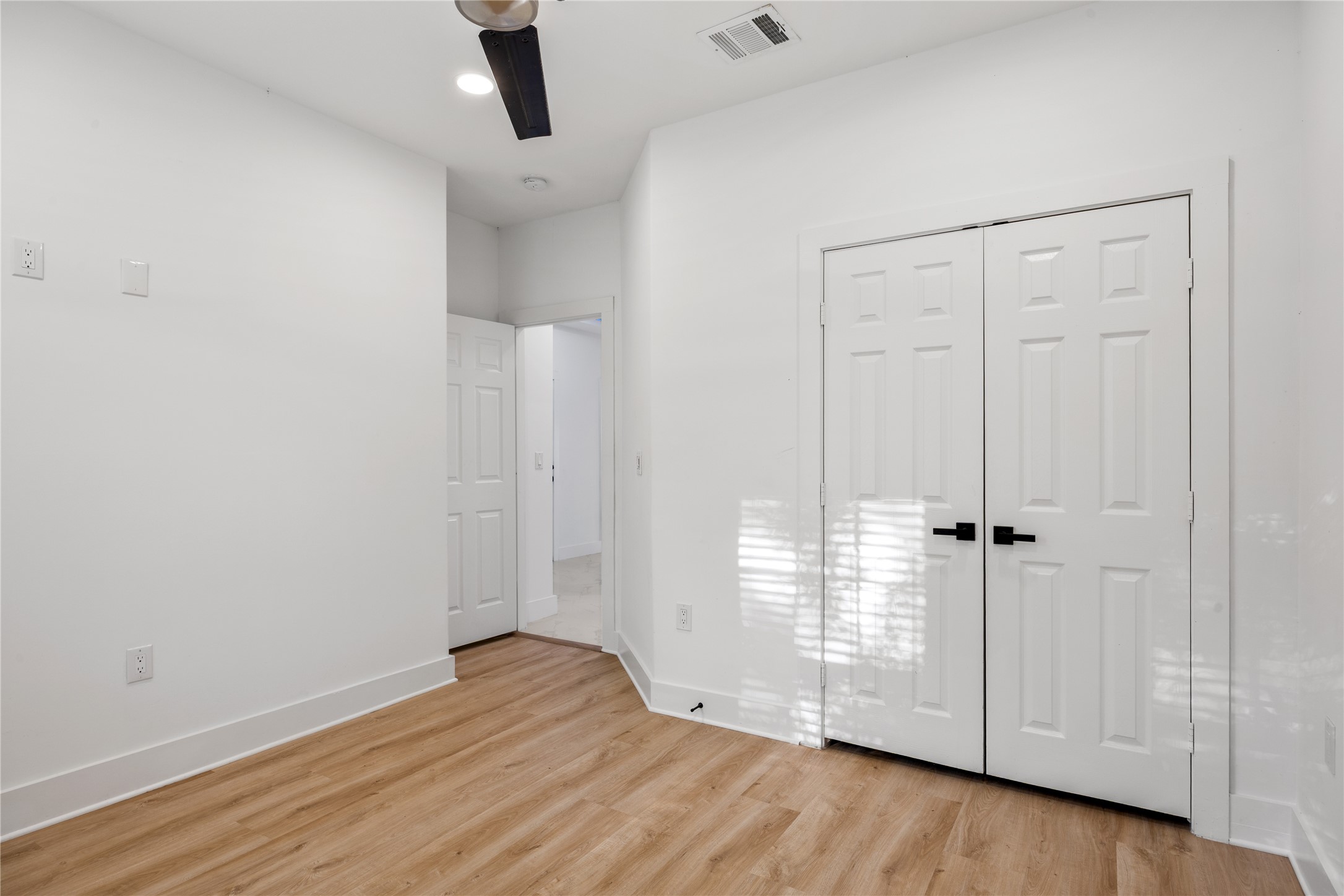 1121 Austin Street Rosenberg, TX 77471 - Photo 8 of 44 This room features a clean, modern design with white walls and luxury vinyl flooring, accented by a ceiling fan and recessed lighting. It includes a double-door closet for ample storage, and a doorway leading to an adjacent space.