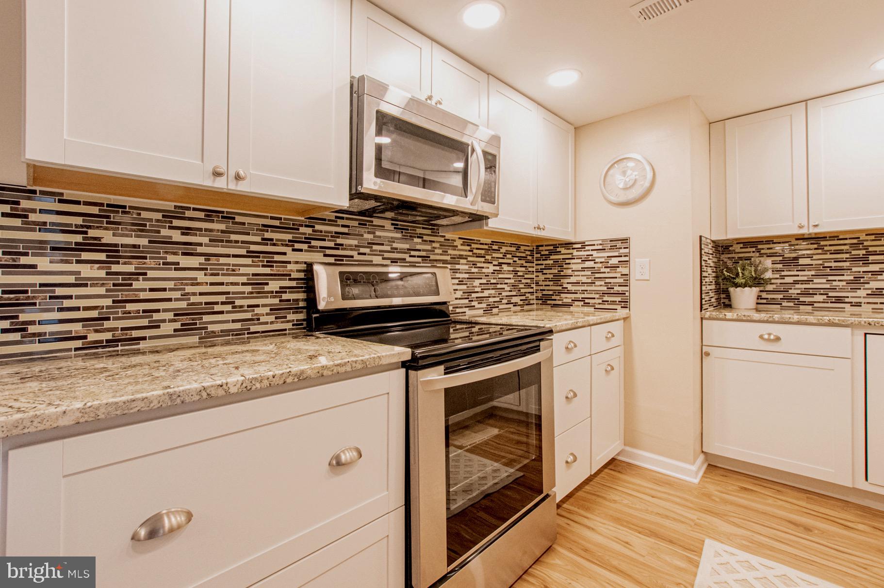a kitchen with stainless steel appliances granite countertop white cabinets and a stove a oven with wooden floor