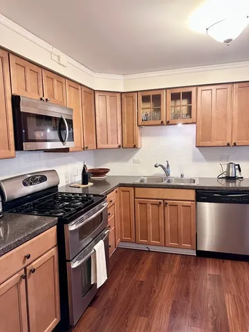 a kitchen with granite countertop wooden floors wooden cabinets and stainless steel appliances