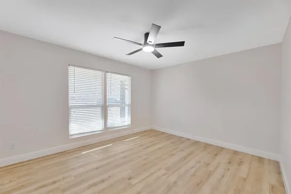 an empty room with wooden floor ceiling fan and windows