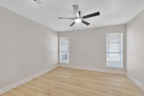 an empty room with wooden floor fan and windows