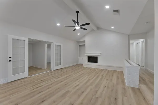 an empty room with wooden floor a ceiling fan a fireplace and windows