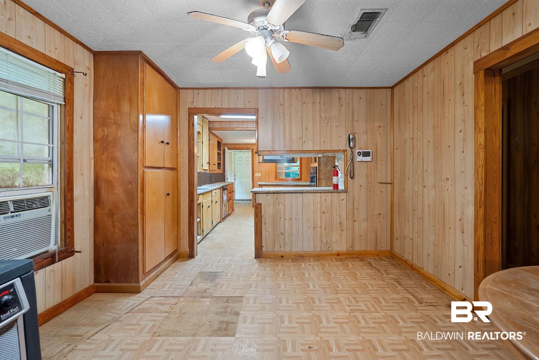 18318 Kendrick Road Robertsdale, AL 36567 - Photo 12 of 39 Wood-paneled room featuring patterned flooring, a ceiling fan with integrated lighting, a pass-through window opening to an adjacent area, and built-in wood cabinetry