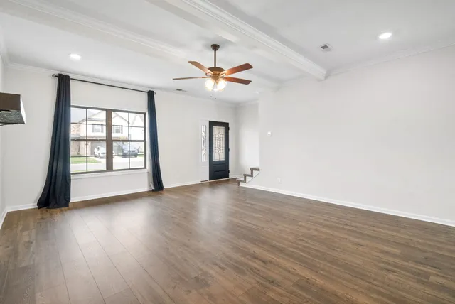 a view of an empty room with wooden floor and a kitchen view