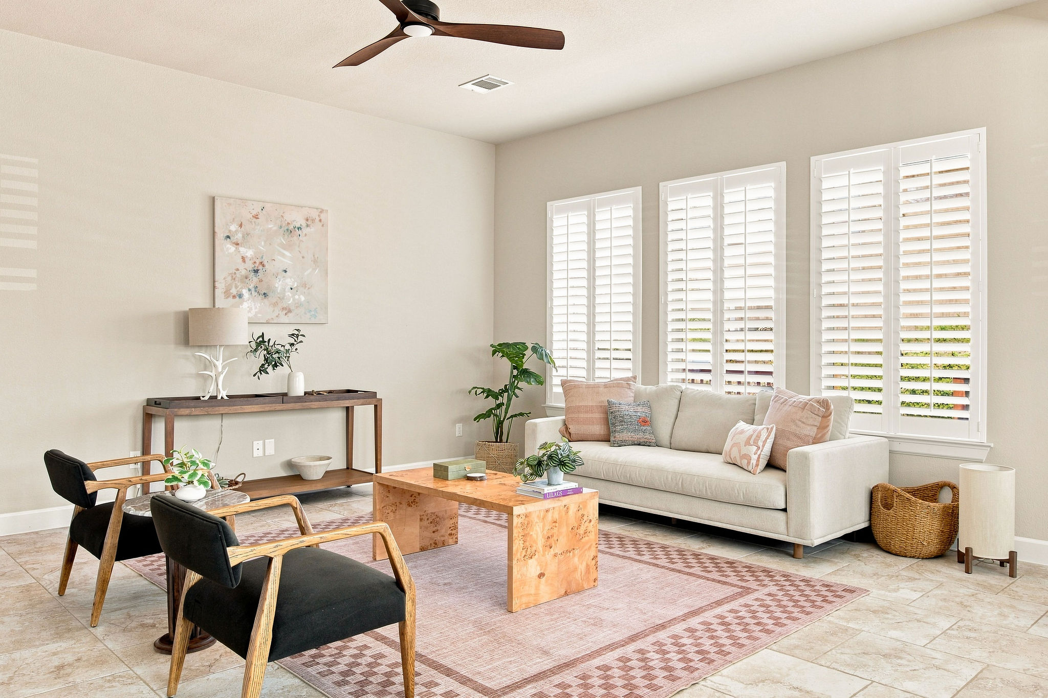 Sunlight streams through plantation shutters onto the elegant tile flooring of this comfortable living space.
