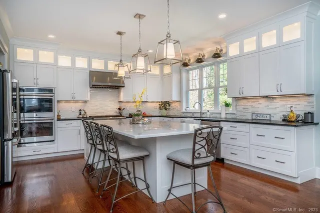 a kitchen with stainless steel appliances granite countertop a stove top oven a sink a dining table and chairs with wooden floor