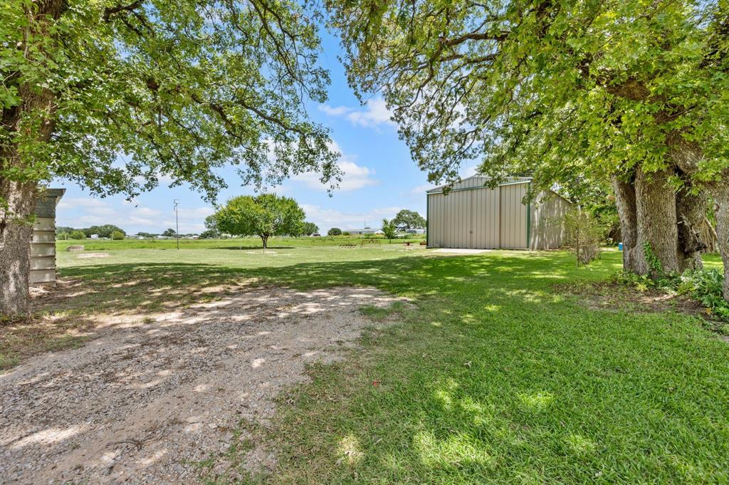 515 New Highland Road Springtown, TX 76082 - Photo 29 of 38 Expansive outdoor property featuring a substantial metal outbuilding, gravel drive, and mature trees providing natural shade