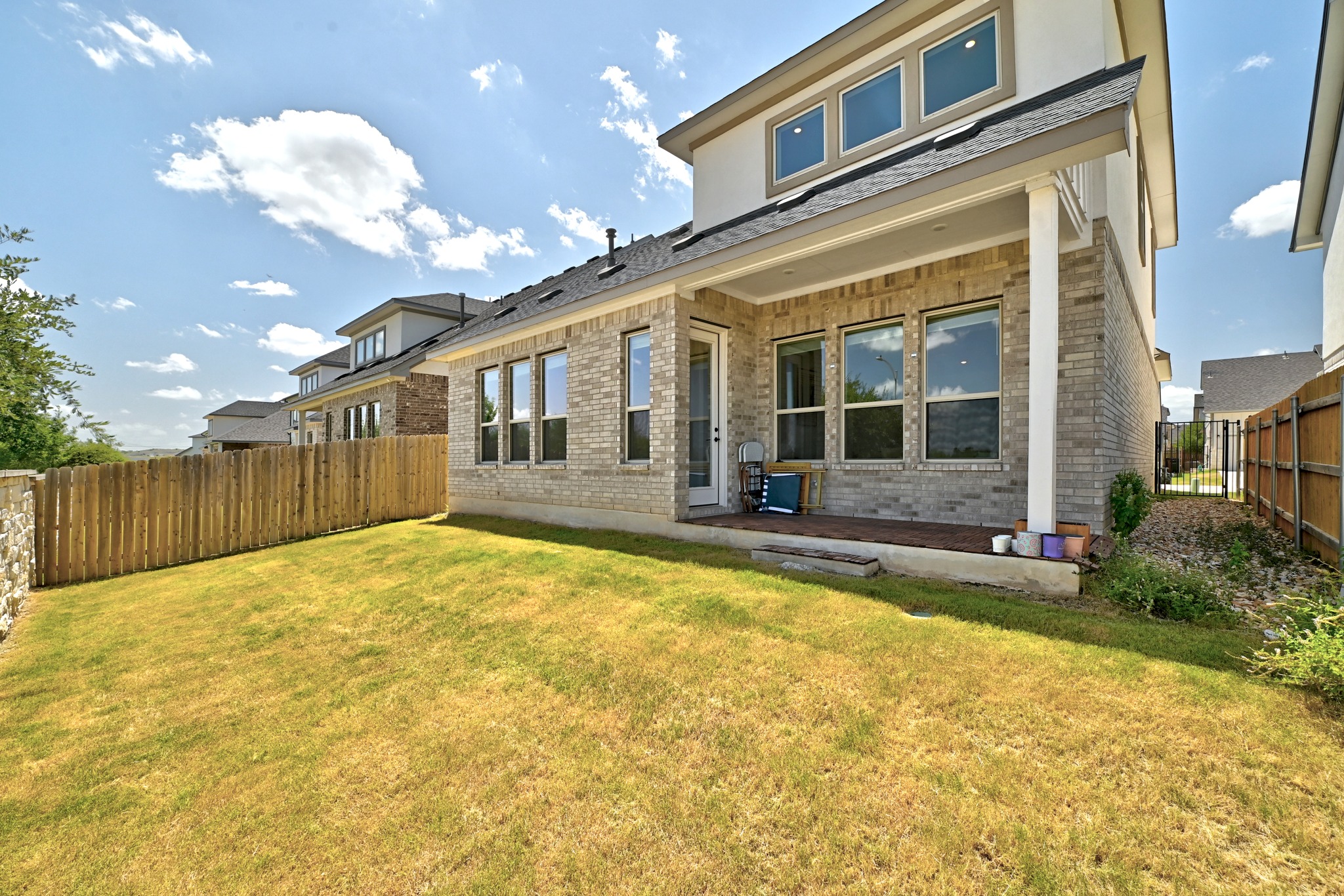 2702 Sebring Circle Austin, TX 78747 - Photo 27 of 35 A grassy backyard features a covered brick patio under a bright, partly cloudy sky.