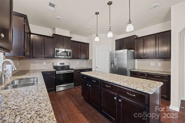 a kitchen with stainless steel appliances granite countertop a sink a stove top oven a refrigerator cabinets and wooden floor