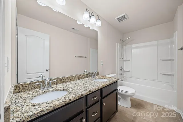 a bathroom with a granite countertop double vanity sink a mirror and a bathtub