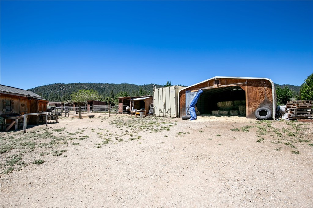10960 Steinhoff Road Frazier Park, CA 93225 - Photo 13 of 46 A functional ground-level shot showcasing a spacious, rustic wooden outbuilding with a wide open-front entry. Perfect for storing ranch equipment, feed, or tools, this structure sits alongside fenced corral areas with a scenic mountain backdrop.