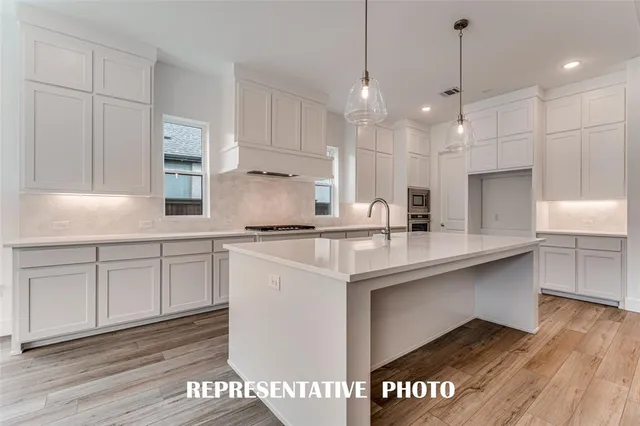a large white kitchen with granite countertop a stove and a wooden floor