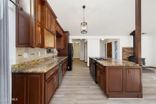 a kitchen with stainless steel appliances granite countertop a refrigerator a sink dishwasher a stove and a dining table with wooden floor