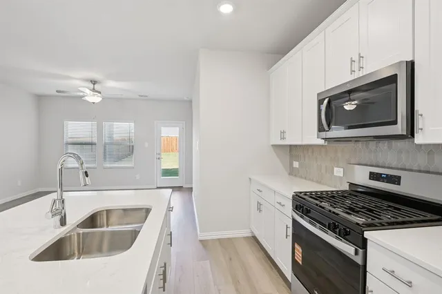 a kitchen with white cabinets a sink stove and microwave