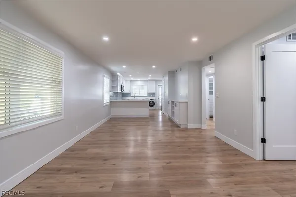 a view of an empty room and kitchen with wooden floor