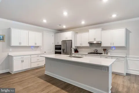 a large kitchen with stainless steel appliances granite countertop a stove a sink a refrigerator and white cabinets granite countertops with wooden floor