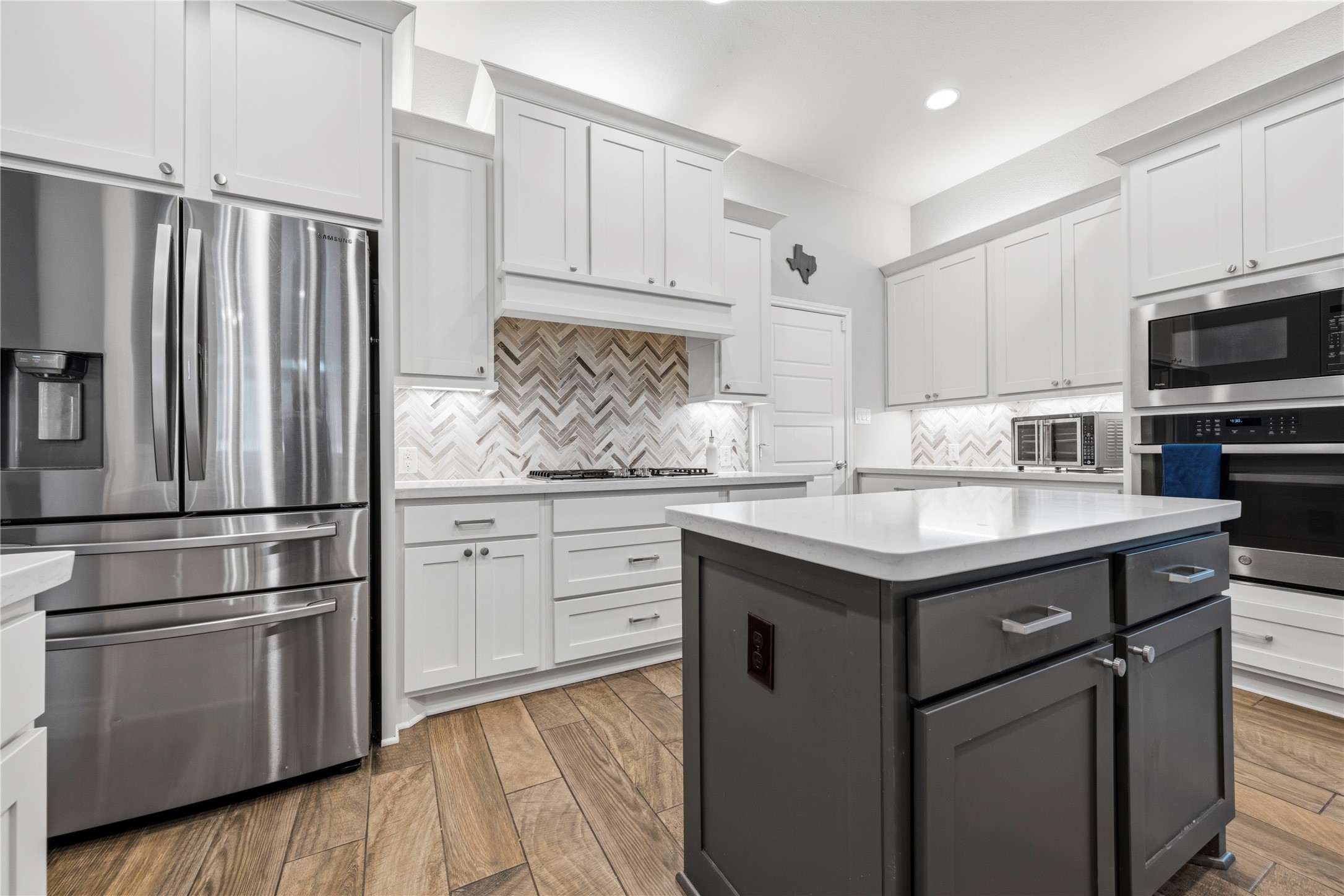 140 Catani Loop Georgetown, TX 78628 - Photo 16 of 36 A contemporary kitchen features sleek stainless steel appliances, pristine white cabinetry, and an eye-catching herringbone tile backsplash.
