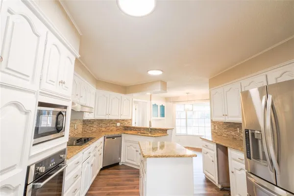a kitchen with stainless steel appliances granite countertop a refrigerator a stove and a sink with wooden floor