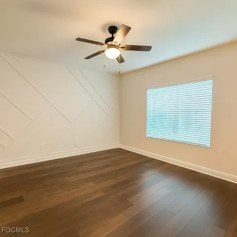 an empty room with wooden floor chandelier fan and windows